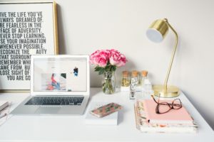 A home desk with pink notebooks and a gold lamp